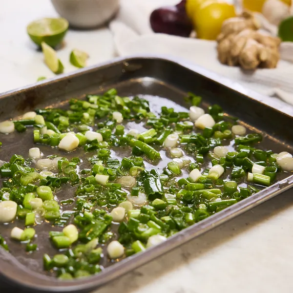 Baking tray with chopped green vegetables, herbs, and limes on a white surface.
