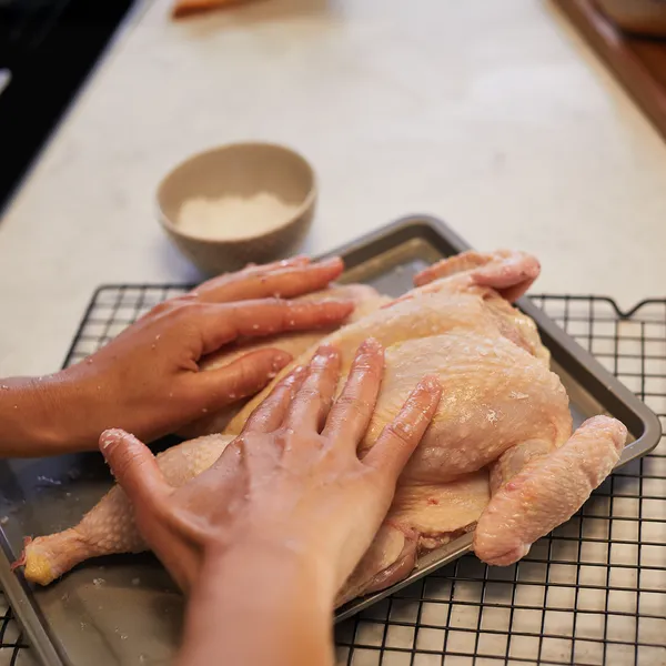Hands preparing a whole raw chicken on a baking sheet with a wire rack