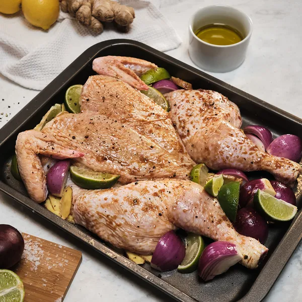 Roasted chicken thighs with vegetables, lemon, and ginger on a baking sheet.
