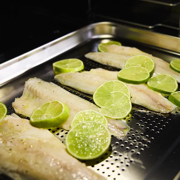 Baked fish fillets with lime slices on a metal baking tray in the oven.