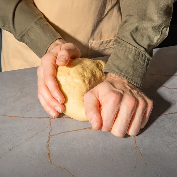 Hands kneading dough on a cracked stone surface, preparing homemade bread.
