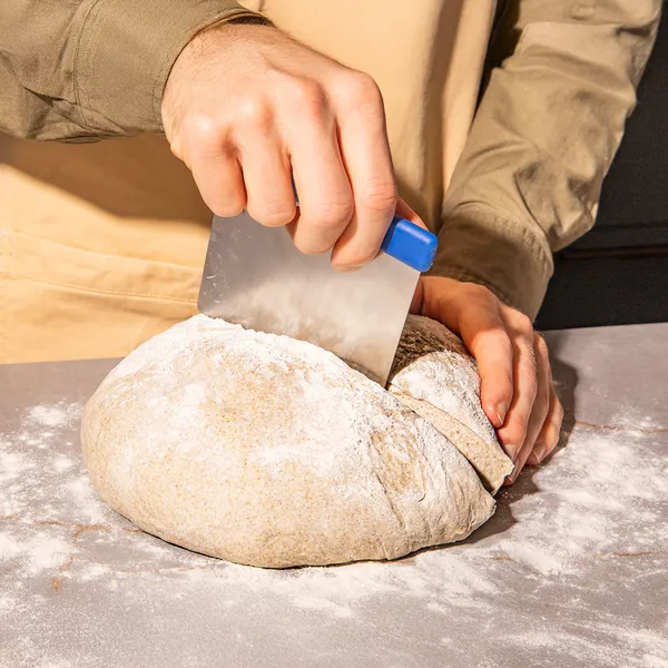 Hands kneading and cutting freshly baked bread on a floured surface.
