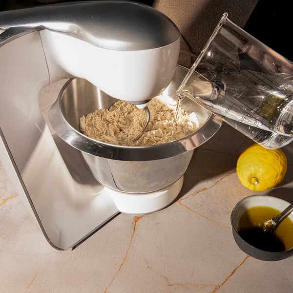 Kitchen appliance mixing dough, lemon, and cooking ingredients on counter.