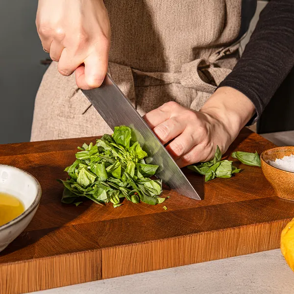 Hands chopping fresh spinach leaves on a wooden cutting board, with olive oil and salt nearby.