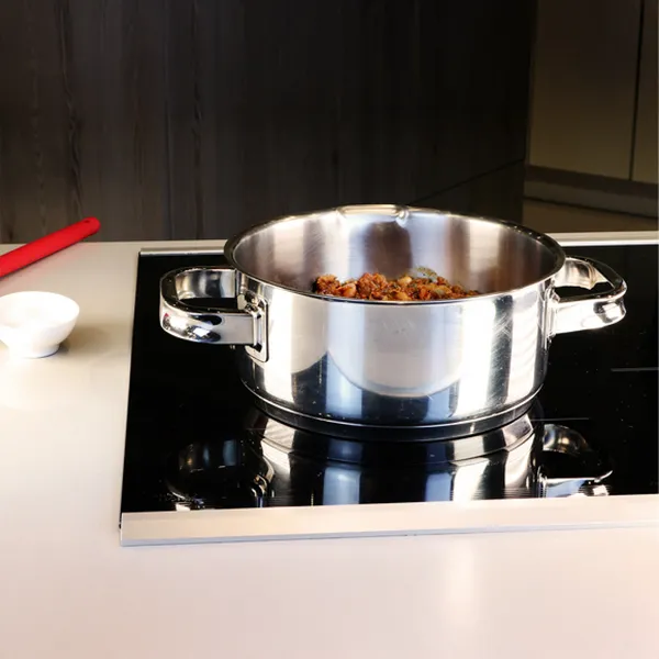 Stainless steel pot with cooked food inside on a black stovetop in a modern kitchen setting.