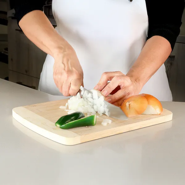 Person chopping onions on a wooden cutting board with halved green chili and whole onions nearby in a kitchen.