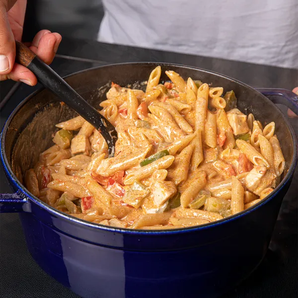 Pan of creamy penne pasta with chicken, red and green bell peppers, garnished with fresh herbs.