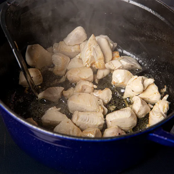Chunks of chicken cooking and sizzling in a blue cast iron pot with steam rising from the hot oil.
