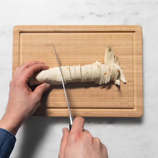 Person slicing a peeled banana into even pieces on a wooden cutting board over a white marble surface.