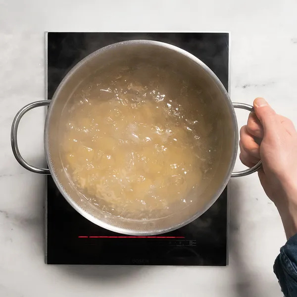 Hand holding a pot with boiling water on an induction cooktop.