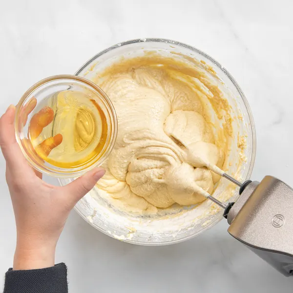 Person pouring apple cider into a mixing bowl with dry ingredients to make baked apple cider donut batter