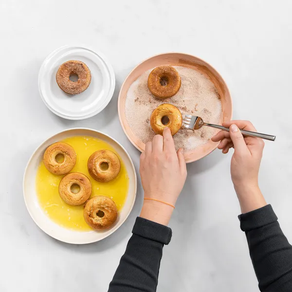 Hand dipping a baked donut into melted butter and cinnamon sugar to coat before serving