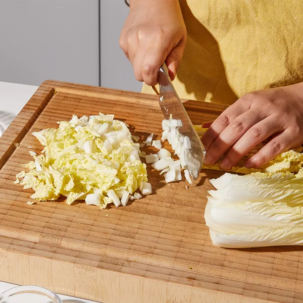 Person chopping napa cabbage on a wooden cutting board with a large knife.