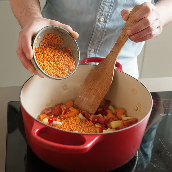 Open fridge with lidded plastic containers on the top shelf, cans and beer bottles and cartons on the middle shelves.