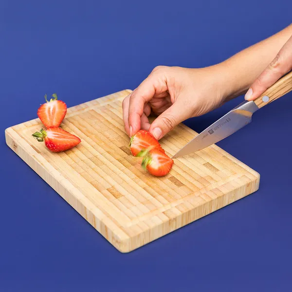 Hand slicing a strawberry on a wooden cutting board against a blue background.