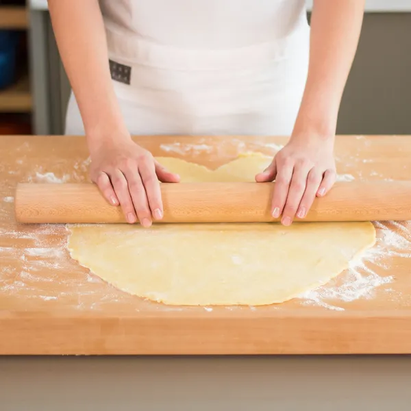 Hands spreading ceramic baking beans on parchment paper in a baking dish on a striped cloth