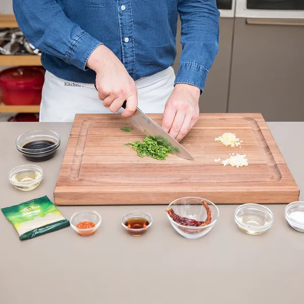 Dicing Person chopping green herbs on a wooden cutting board with small piles of minced garlic and various small bowls of spices and liquids arranged around the boardon a cutting board