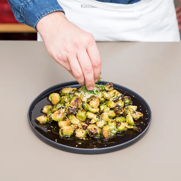 Hand sprinkling seasoning over roasted Brussels sprouts on a black plate