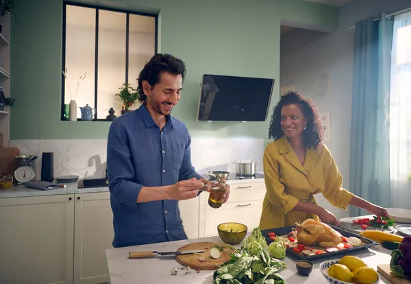  Person wiping induction cooktop with yellow cloth, Bosch cleaning bottle on counter, purple "XX% CLEANING DAYS" badge top-left.