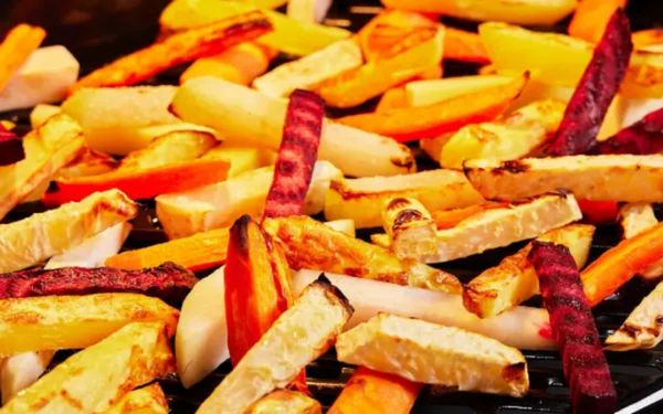 Ger&ouml;stete, bunte Gem&uuml;sest&auml;bchen, darunter Karotten, Rote Bete und Pastinaken, auf einem schwarzen Grillblech.