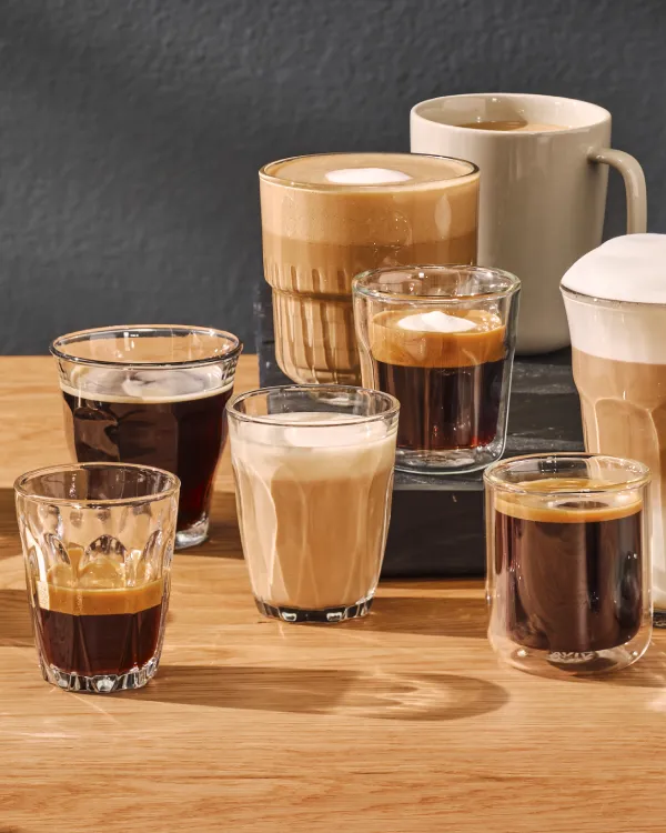 En mängd olika kaffedrycker inklusive espresso, latte, cappuccino, svart kaffe och iskaffe, visade på en träyta.