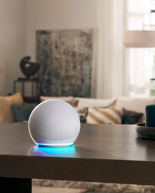 Minimalistisk heminredning med smart högtalare, lampa och konstverk på träbord.