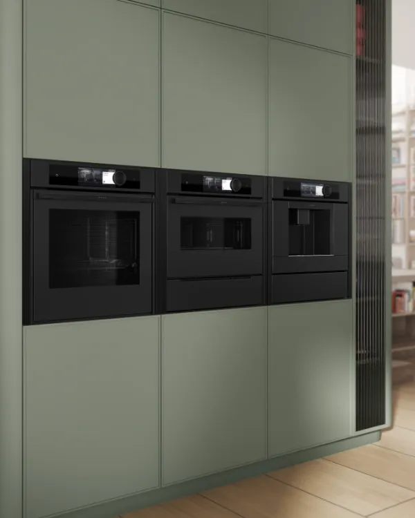 Modern kitchen featuring built-in black appliances integrated into green cabinetry with adjacent shelves holding kitchen utensils.