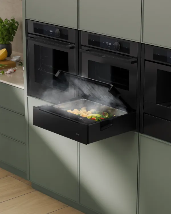 Modern kitchen with built-in black steam oven drawer open, steaming food inside, next to a built-in coffee machine.