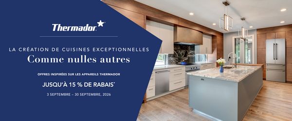 Cuisine blanche moderne avec un grand &icirc;lot central, robinetterie dor&eacute;e, cuisini&egrave;re au bouton bleu et portes ouvertes donnant sur un jardin.