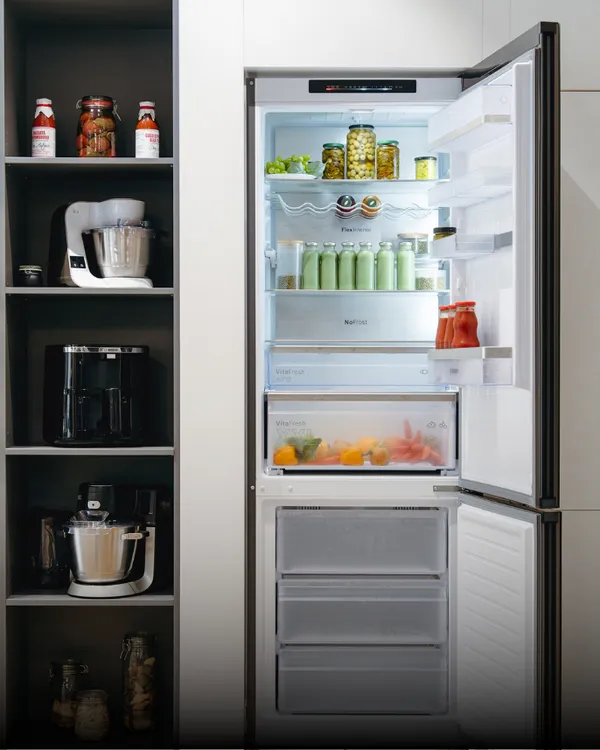 Bosch beépíthető hűtő nyitott ajtóval, a belsejében gyümölcsökkel és zöld smoothiekkal.