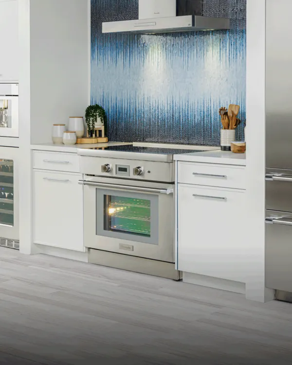 Bright modern kitchen with Thermador stainless steel appliances, white cabinets and a blue tiled backsplash