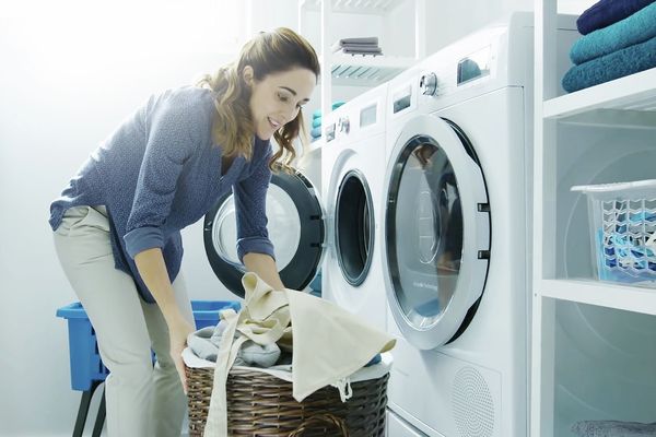 Uma mulher a clocar roupa na máquina de lavar e de secar Home Connect com um sorriso nos lábios