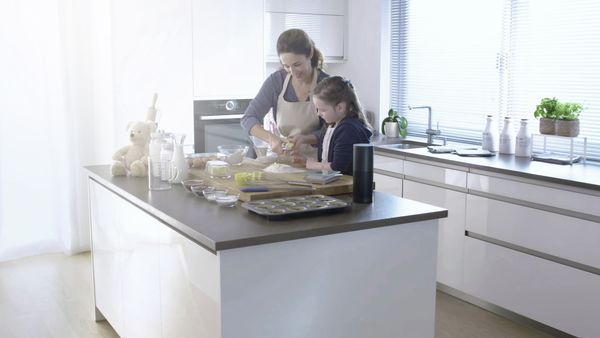 Maminka pečící se svým dítětem s použitím služby Amazon Alexa připojené k pečicí troubě s funkcí Home Connect.
