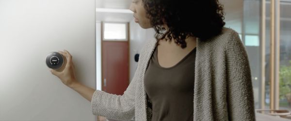 A woman changing the settings on a Nest thermostat that is connected to Home Connect