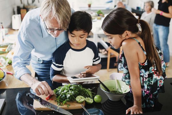 Man och två små barn i kök tittar på nyskurna grönsaker