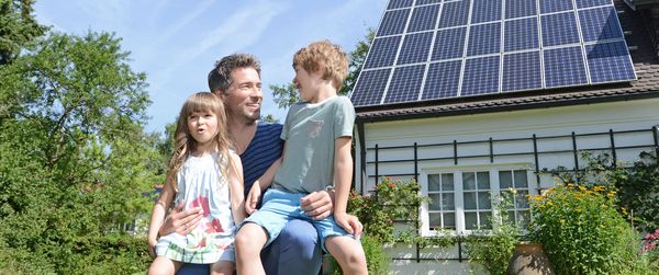 Чоловік з двома дітьми, за ним - будинок з сонячними батареями на даху.