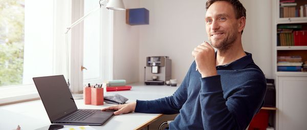A man sits at his desk in front of a laptop in his home office.