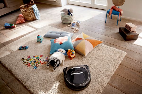 Roxxter cleaning a childrens room, in which toys are laying on a carpet.