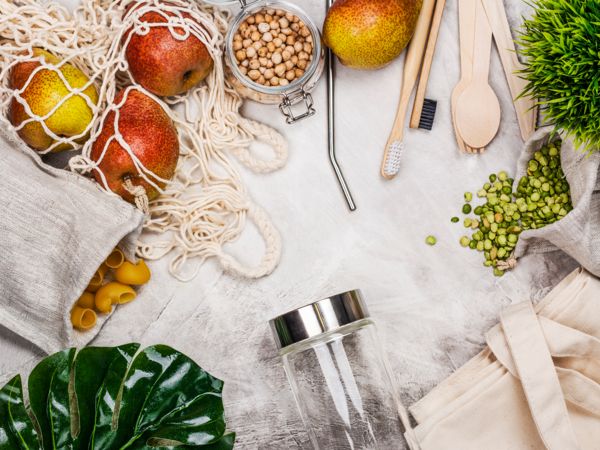 Sacchetti della spesa riutilizzabili con frutta, pasta, ceci, utensili in legno, spazzolino da denti in bamb&ugrave;, paglia di metallo e un barattolo di vetro.