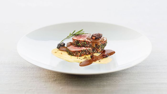 Wit bord met twee plakjes kalfshaas, gegarneerd met een aardappelpuree, jus en een takje rozemarijn.