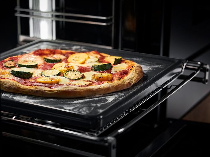 Pizza in uscita da un forno di casa sulla sua teglia