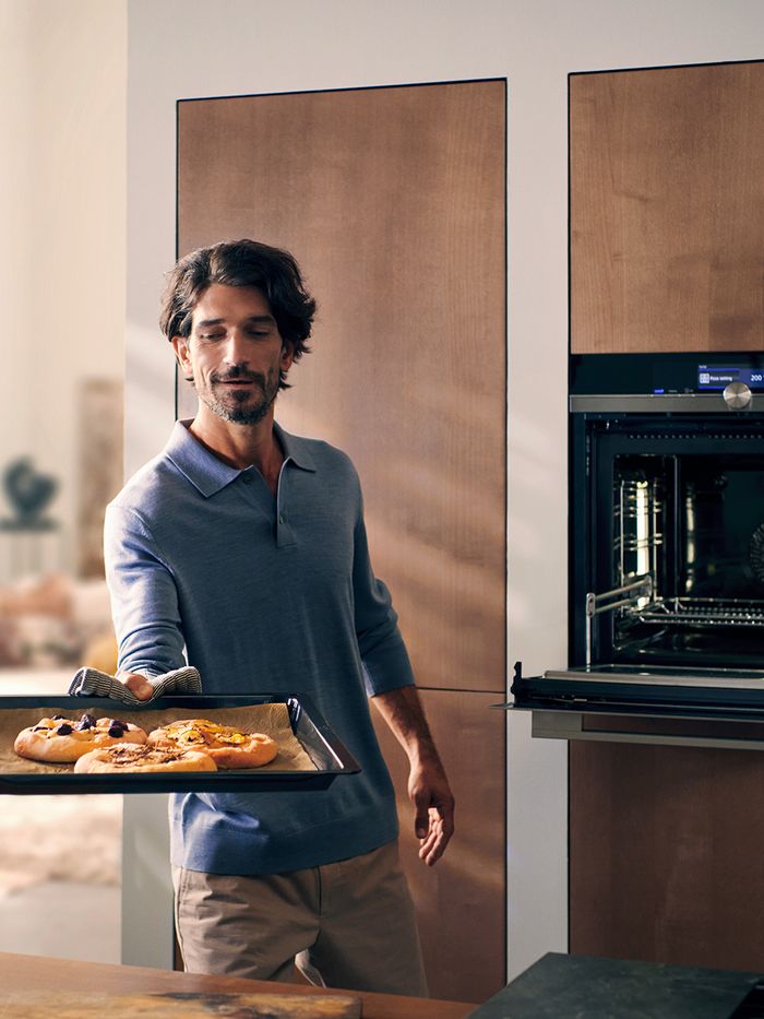 Giovane uomo estrae dal forno una teglia con delle pizze appena sfornate