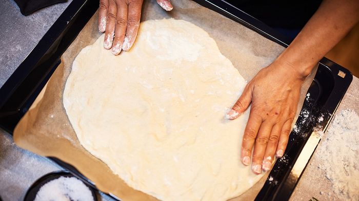 Mani che stendono un impasto su teglia con carta da forno