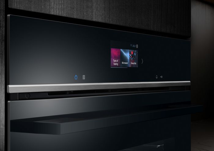Detailní záběr na moderní černý ovládací panel trouby s dotykovým displejem, možnostmi typu ohřevu a nastavení mikrovln.