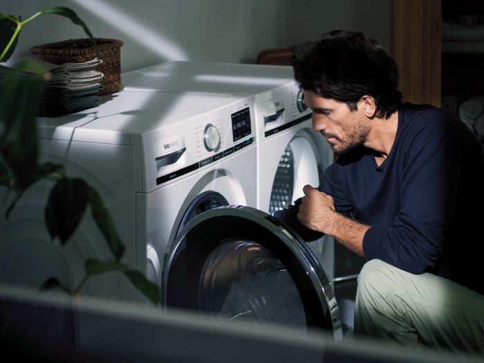 Der Mann untersucht die Waschmaschine im beleuchteten Raum.