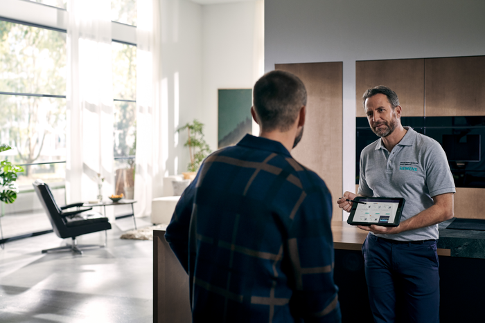 Siemens Kundendienst-Techniker erklärt einem Kunden die Gerätefunktionen auf einem Tablet in moderner Wohnküche.