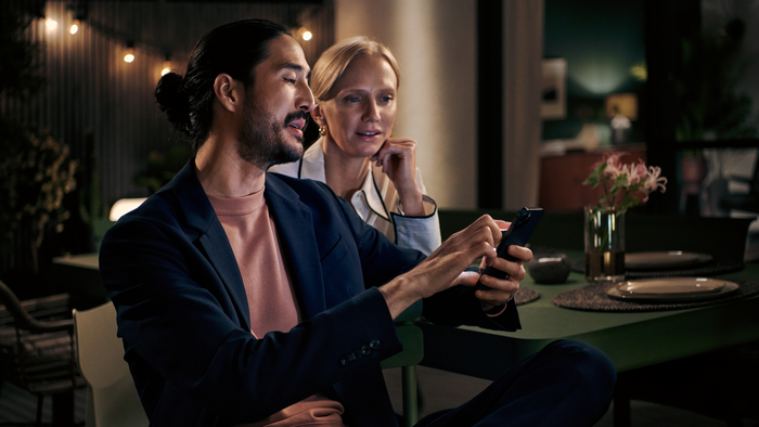 Mężczyzna i kobieta siedzący przy stole w jadalni, patrzący na smartfon trzymany przez mężczyznę.