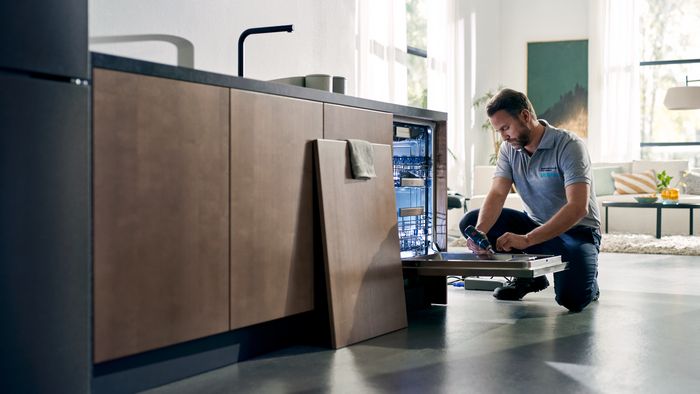 Man hurken op de vloer, repareren of installeren van keukenapparatuur.
