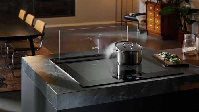 Isola cucina moderna con piano cottura a induzione Siemens, pentola in utilizzo e sistema di aspirazione integrato nel piano