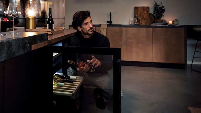 Giovane uomo che sceglie una bottiglia di vino dalla sua cantinetta Siemens in cucina